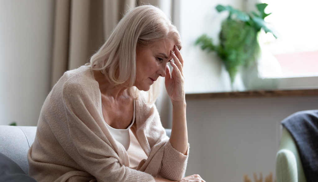 Eldre dame sitter i sofaen og tenker og ser bekymret ut