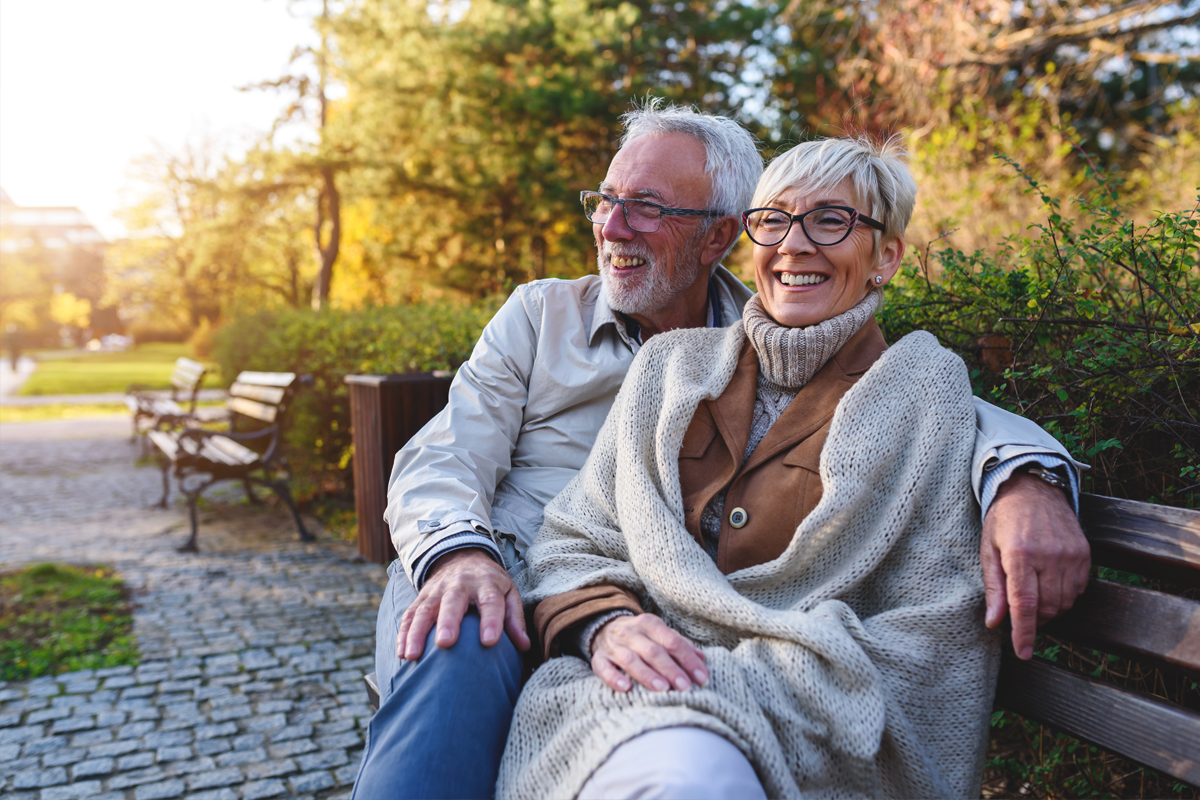 Eldre parr sitter på en benk i en park og holder rundt hverandre og smiler