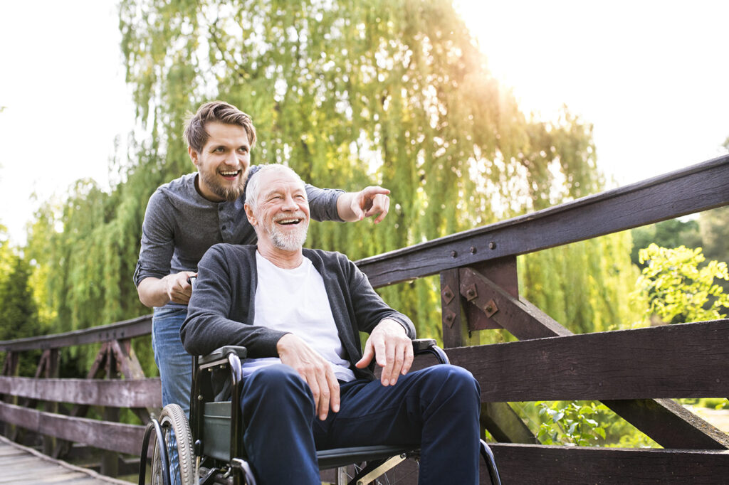 Eldre mann i rullestol blir hjulpet av ung mann