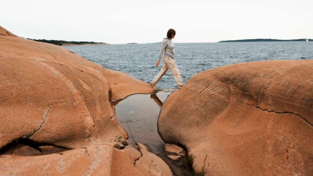 Sommeridyll ved kysten – en person i bevegelse mellom varme svaberg under åpen himmel.